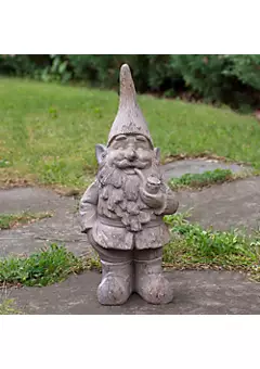 Concrete garden gnome statue with pointed hat, standing on a stone path surrounded by grass.