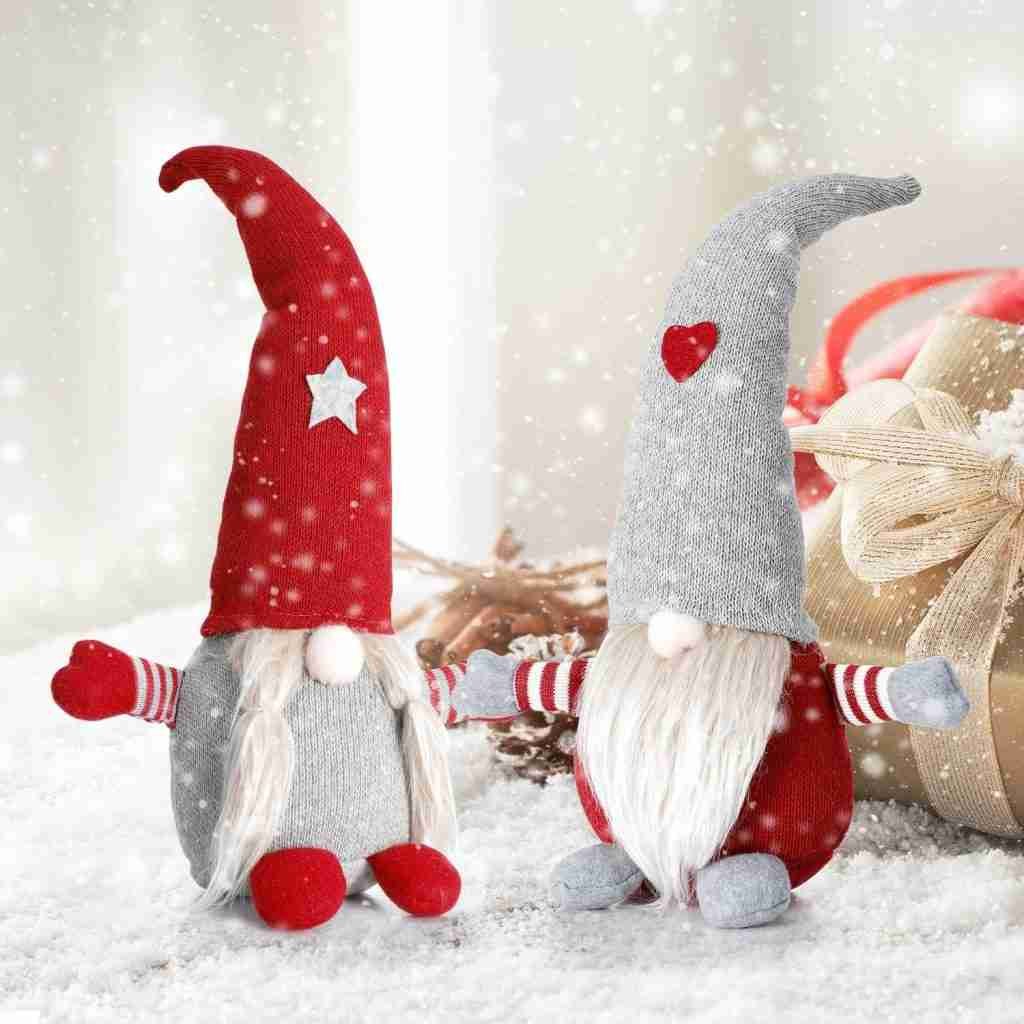 Two Christmas gnome plush decorations in red and grey outfits, sitting on snow with snowflakes falling around.