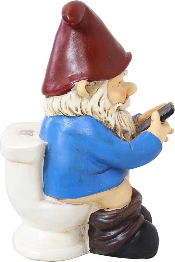 A garden gnome figurine wearing a red hat, blue shirt, and black boots, sitting on a toilet and holding a smartphone.