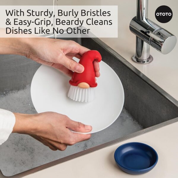 Hand holding a gnome-shaped dish brush with white bristles, scrubbing a white plate in a sink. Text: "With Sturdy, Burly Bristles & Easy-Grip, Beardy Cleans Dishes Like No Other." Logo: "OTOTO."