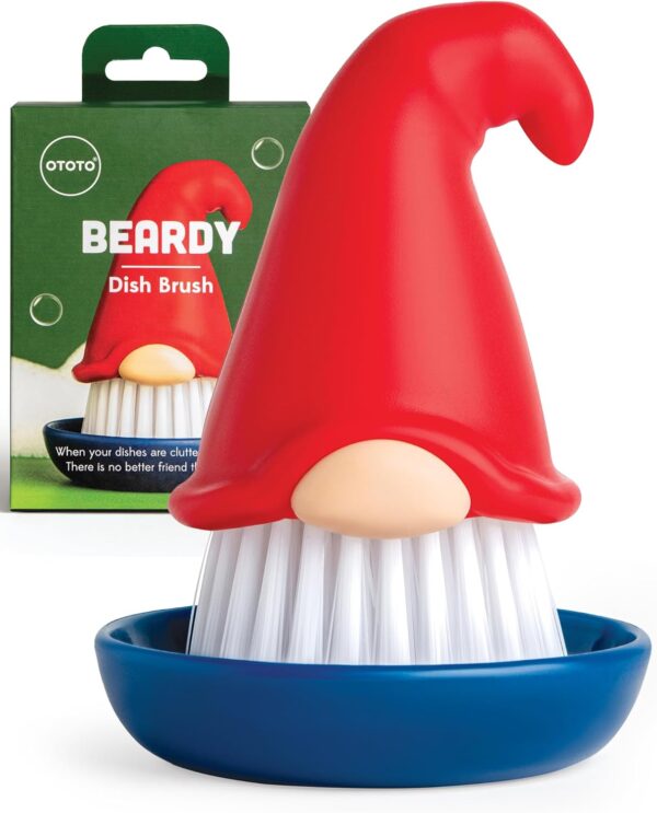 Red gnome-shaped dish brush with white bristles, a red pointy hat, and a beige nose, displayed with its packaging.