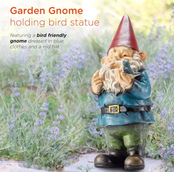 Garden gnome holding a bird statue, standing in a field of purple flowers. Gnome is dressed in blue clothes and a red hat.